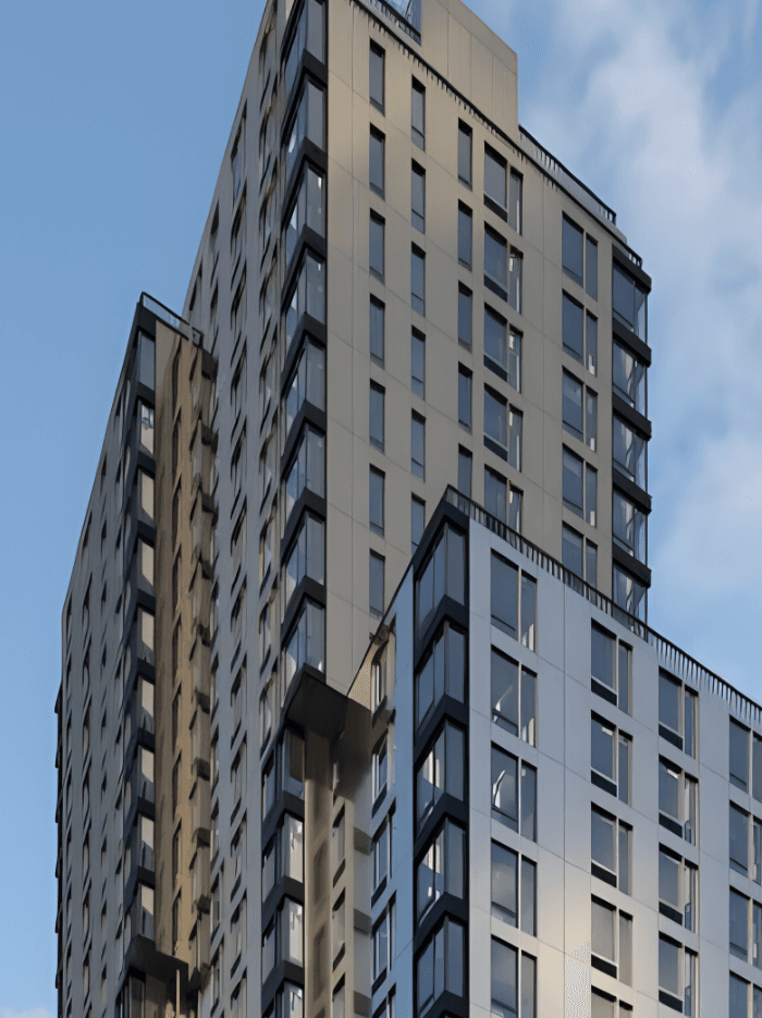 A modern high-rise building with a beige and white exterior stands against a blue sky with a few clouds. The structure features numerous windows and balconies, with varying façade designs that add depth and interest to the architecture.