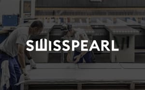 Two workers in an industrial setting handle large sheets of fiber cement material. The word "SWISSPEARL" is prominently displayed in bold white letters in the foreground. The workspace includes tables, tools, and equipment typical of manufacturing or fabrication processes.