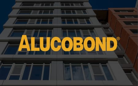 A multi-story building with large windows is shown from a low angle against a blue sky. The word "ALUCOBOND" is prominently displayed in large, yellow letters across the center of the image, highlighting its use of ACM for exterior facade cladding.