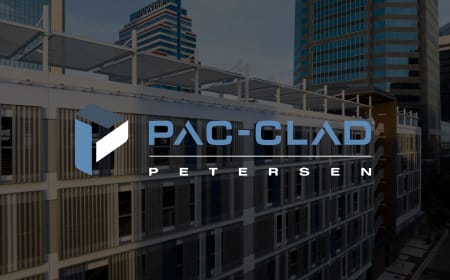 Logo for PAC-CLAD Petersen superimposed on a cityscape background with modern office buildings and sleek exterior facade cladding. The logo features geometric shapes and stylized text in blue and white.