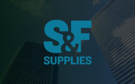 The image displays the logo for "S&F Supplies" in bold blue letters against a backdrop of modern skyscrapers under a clear sky. The ampersand is stylized to connect the "S" and "F" together, reflecting their expertise in exterior facade cladding and ACM.