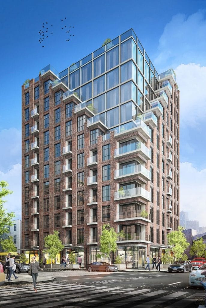 A modern multi-story building stands on a busy street corner. The structure features a mix of brick and glass exteriors, with several balconies protruding from various floors. Pedestrians walk along the sidewalks while cars and electric scooters move on the street below.