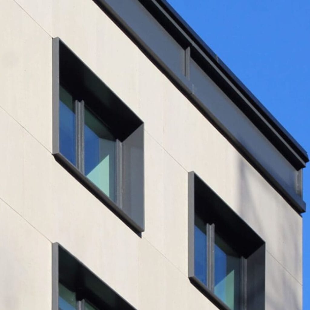 A sleek building facade with large rectangular windows, bordered in dark trim, set against a pale exterior wall. The clear blue sky in the background enhances the modern design.